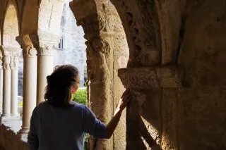 Local person quietly observing the details of an ancient stone arch in a medieval cloister at golden hour, with warm natural light and textured aged stone surroundings.